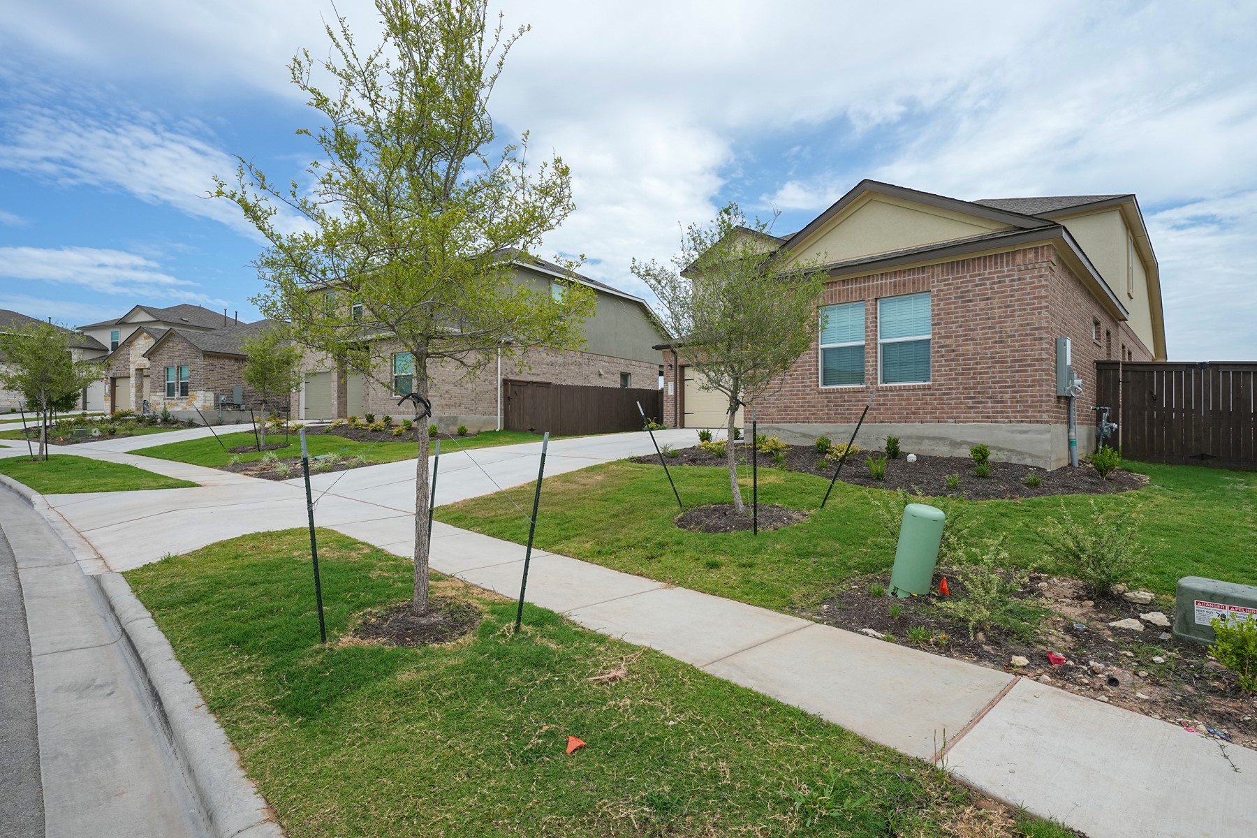 A quiet neighborhood street showcases modern homes with landscaped yards and private fences.