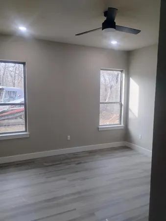 an empty room with wooden floor chandelier fan and windows