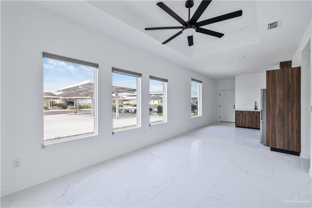 Unfurnished living room featuring a tray ceiling, ceiling fan, healthy amount of natural light, and light marble finish floors