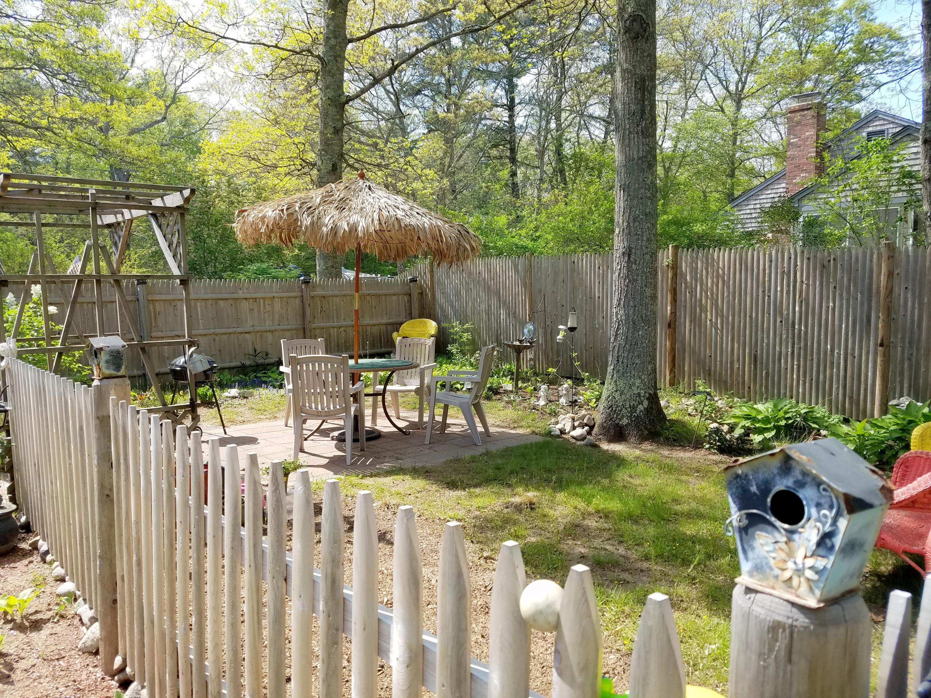 835 Cotuit Road Mashpee, MA 02649 - Photo 3 of 14 a view of a backyard with table and chairs potted plants and covered with wooden fence