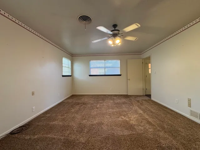 an empty room with a chandelier fan and windows