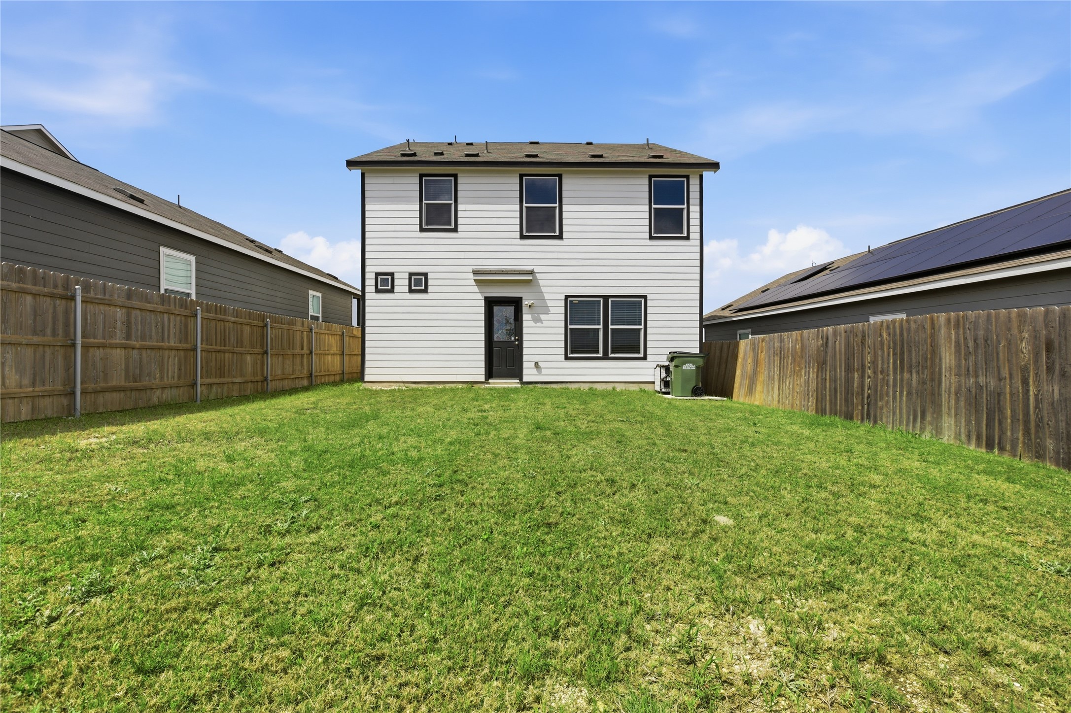 116 Night Riders Way Jarrell, TX 76537 - Photo 32 of 40 Expansive grassy backyard featuring a two-story white siding residence with black-framed windows, a rear entry door, and a brown wood privacy fence
