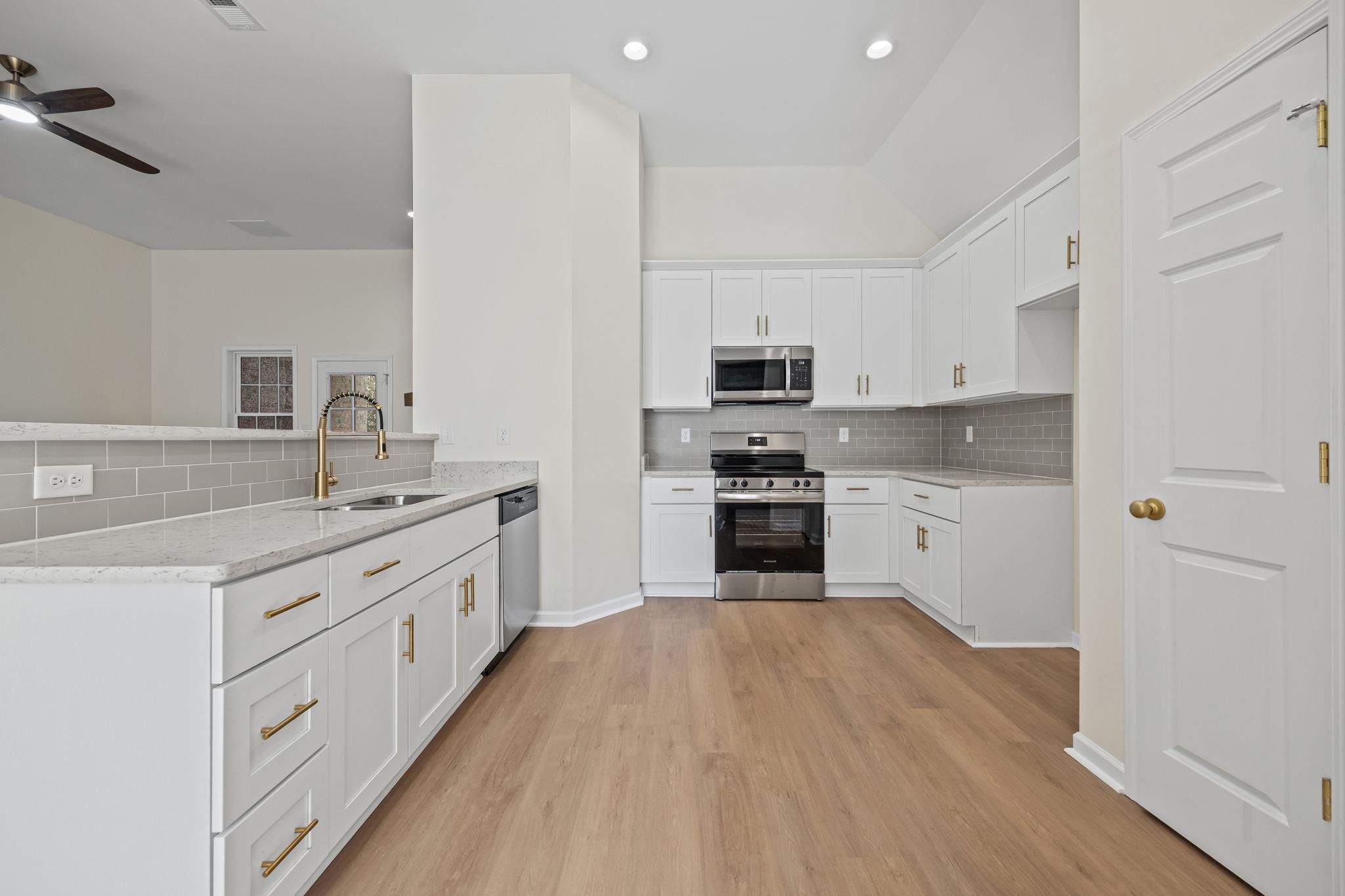 8670 Valmont Circle Memphis, TN 38016 - Photo 11 of 33 Kitchen featuring appliances with stainless steel finishes, white cabinets, tasteful backsplash, vaulted ceiling, and light stone countertops