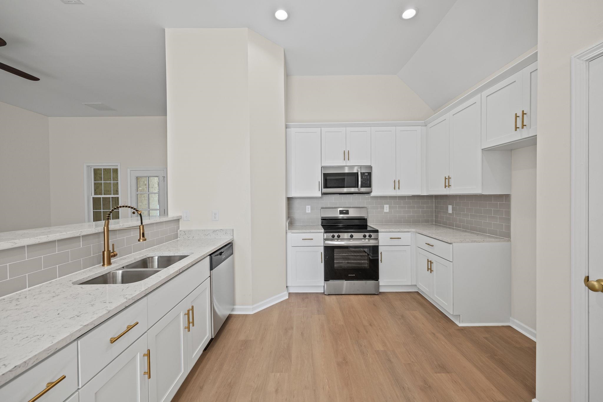 8670 Valmont Circle Memphis, TN 38016 - Photo 12 of 33 Kitchen featuring stainless steel appliances, tasteful backsplash, light stone countertops, white cabinetry, and lofted ceiling