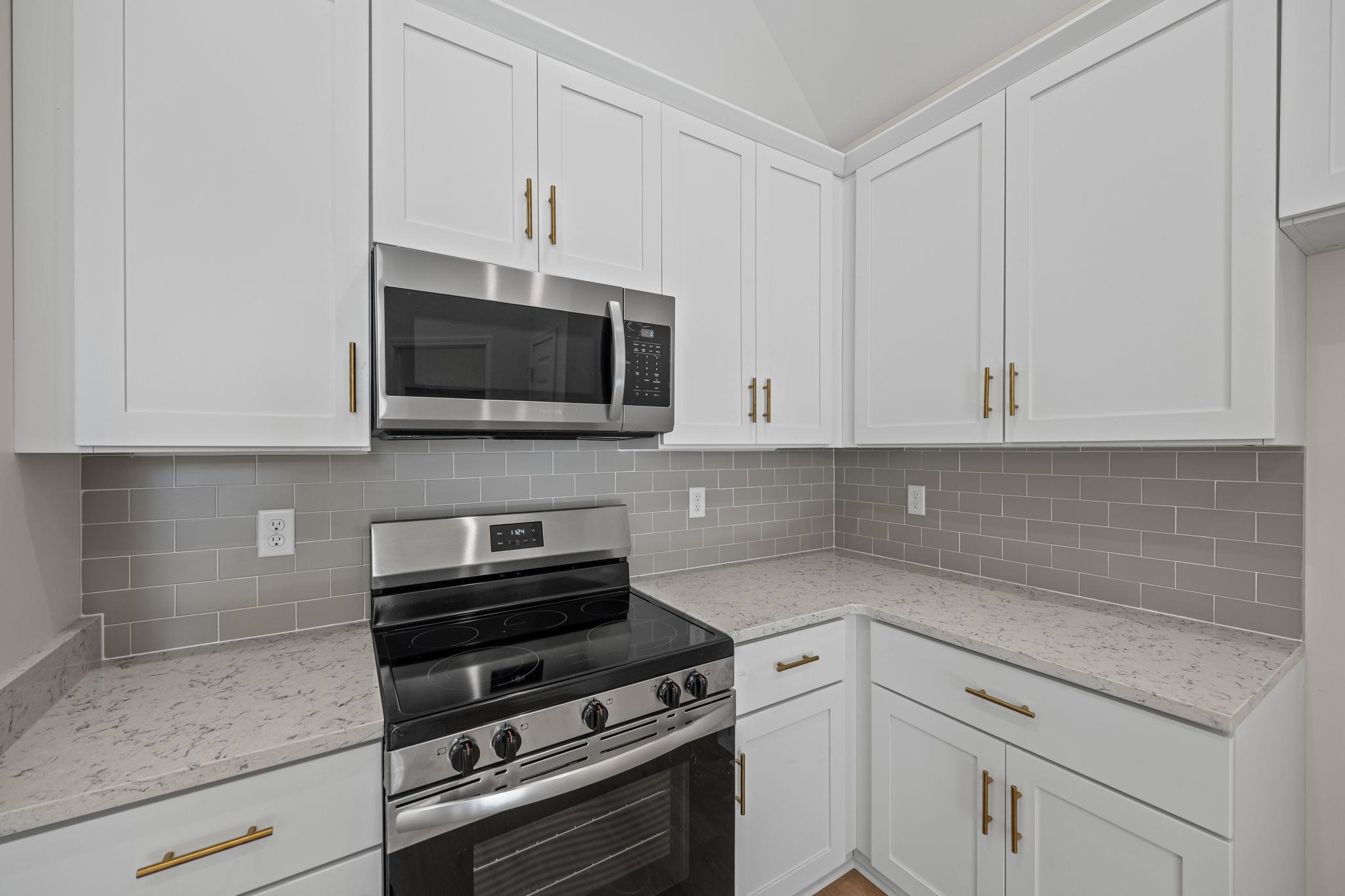 8670 Valmont Circle Memphis, TN 38016 - Photo 15 of 33 Kitchen featuring stainless steel appliances, white cabinetry, light stone counters, backsplash, and vaulted ceiling