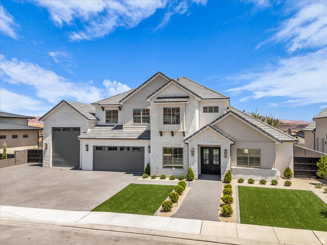 1620 Belayer Drive St. George, UT 84770 - Photo 5 of 51 Contemporary residence featuring a light-colored brick and stucco exterior, dark composite roof shingles, multiple dark garage doors, a double front entry door, and a concrete driveway