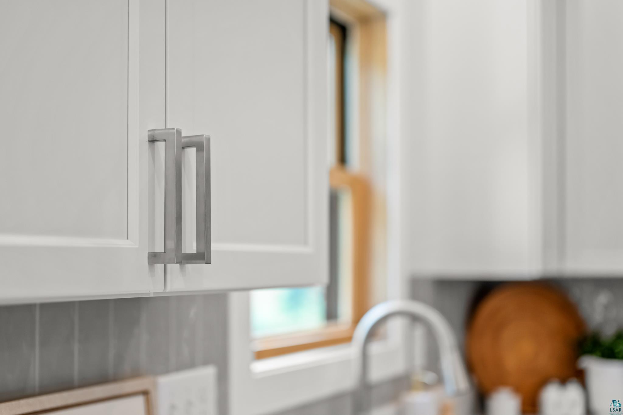 1241 Airport Road Two Harbors, MN 55616 - Photo 22 of 54 White shaker-style cabinetry with rectangular hardware, gray tile backsplash, and a stainless steel faucet