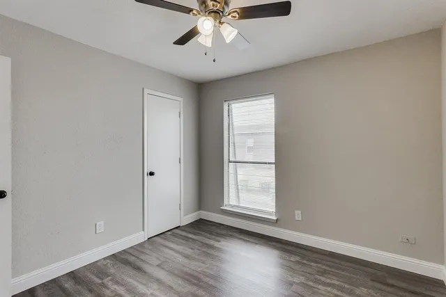 an empty room with wooden floor chandelier fan and windows