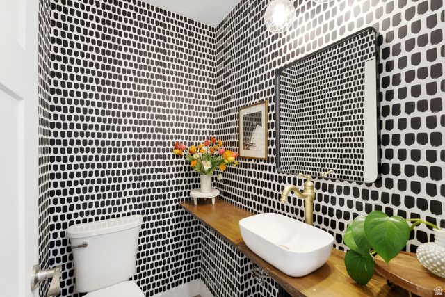 7935 Mustang Loop Road Park City, UT 84098 - Photo 27 of 60 Powder room featuring striking patterned wallpaper, a floating wood-finish vanity with an oval vessel sink, a matte black-framed mirror, and a brass faucet