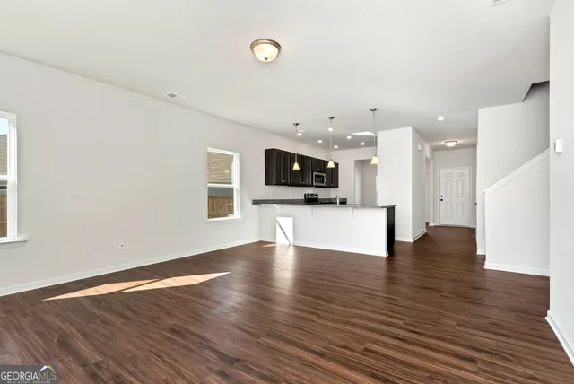 a view of an empty room with wooden floor and a kitchen