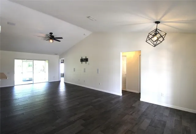 an empty room with wooden floor chandelier fan and windows