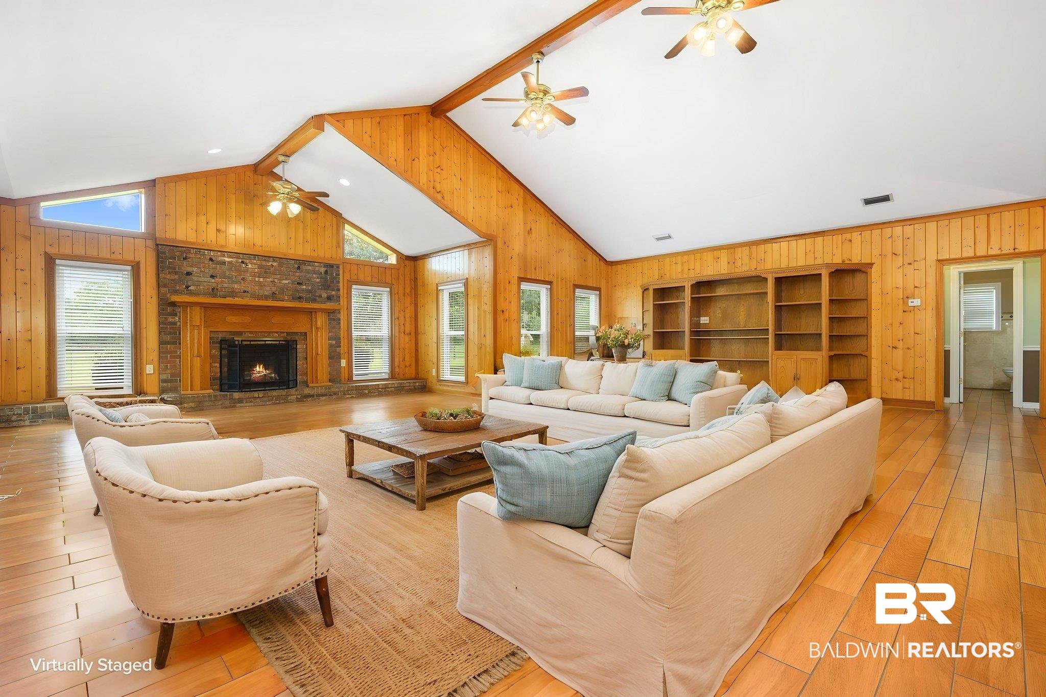 7540 2 Mile Road Irvington, AL 36544 - Photo 5 of 82 Expansive living space featuring a vaulted ceiling with exposed beams, wood-finish flooring, a stone fireplace with a wood mantle, multiple large windows, and built-in shelving