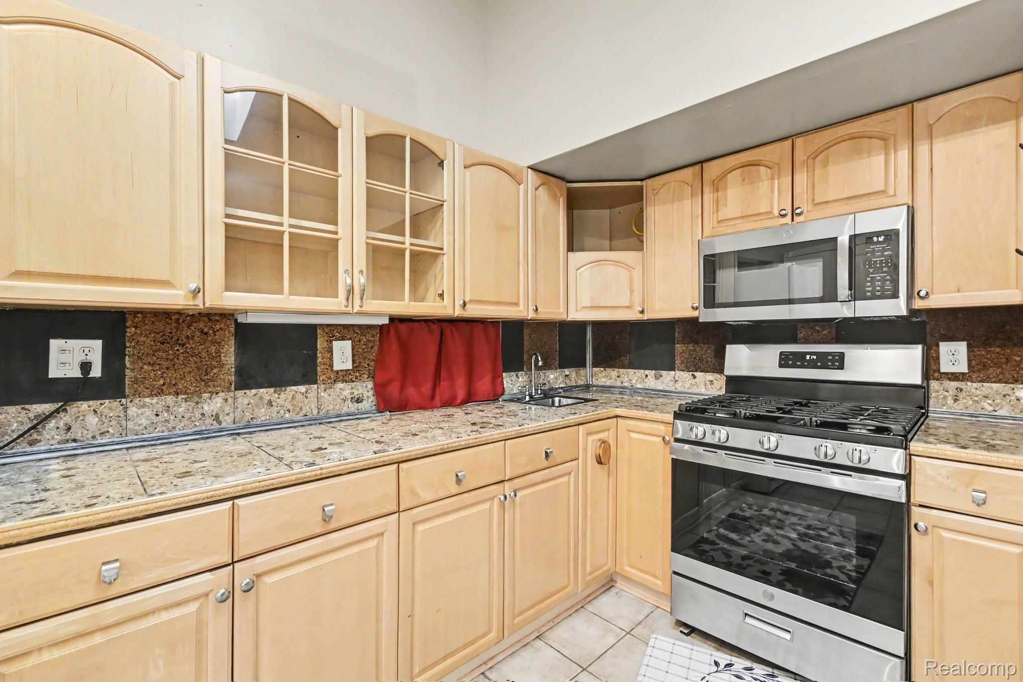 4815 Lytle Road Corunna, MI 48817 - Photo 11 of 31 Kitchen featuring extensive natural wood-finish cabinetry, stainless steel oven with gas cooktop, stainless steel built-in microwave, tiled countertops, and a patterned backsplash