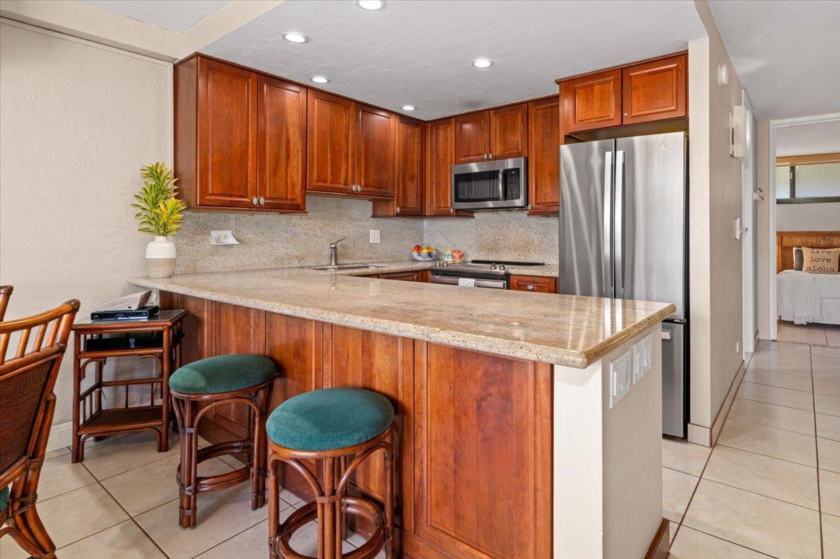 3543 Lower Honoapiilani Road, Unit J302 Lahaina, HI 96761 - Photo 35 of 44 a kitchen with stainless steel appliances granite countertop a table chairs in it and wooden floors