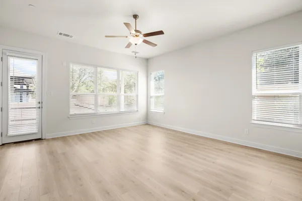an empty room with wooden floor chandelier fan and windows