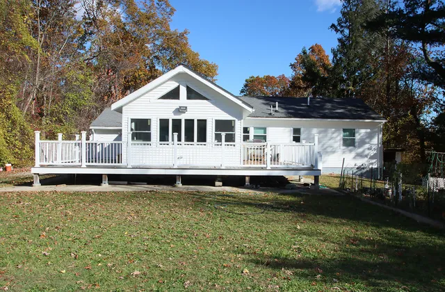 a white house with a large pool and lawn chairs under large trees
