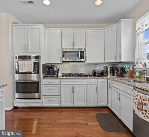 a kitchen with a refrigerator a sink dishwasher a stove and white cabinets with wooden floor