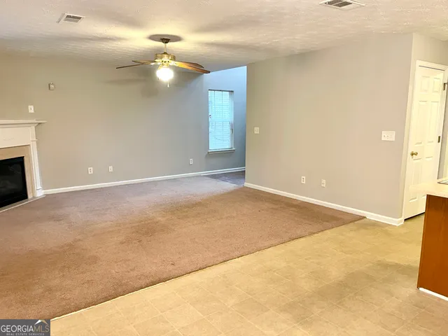 a view of an empty room with window and a kitchen view