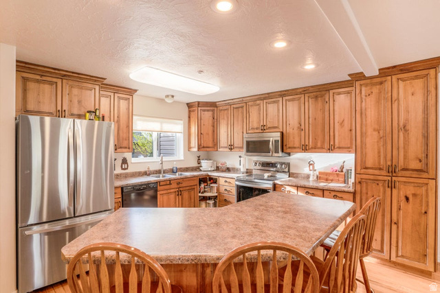 48 South Sage Road Pine Valley, UT 84781 - Photo 17 of 61 Kitchen featuring wood cabinetry, stainless steel appliances, a corner sink with window, recessed lighting, and a breakfast bar with stone-finish countertop
