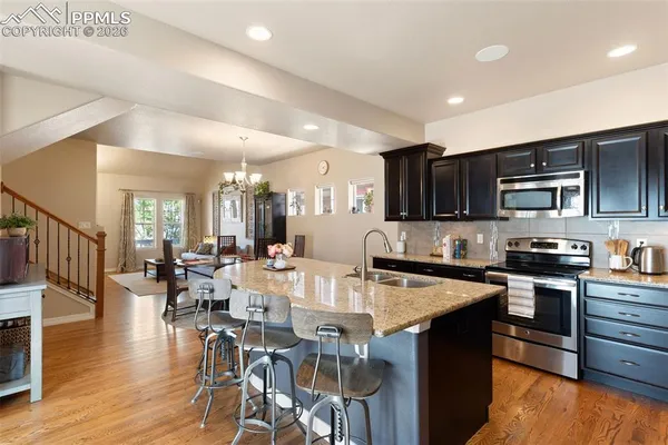 a kitchen with stainless steel appliances granite countertop a stove top oven a sink dishwasher a dining table and chairs with wooden floor
