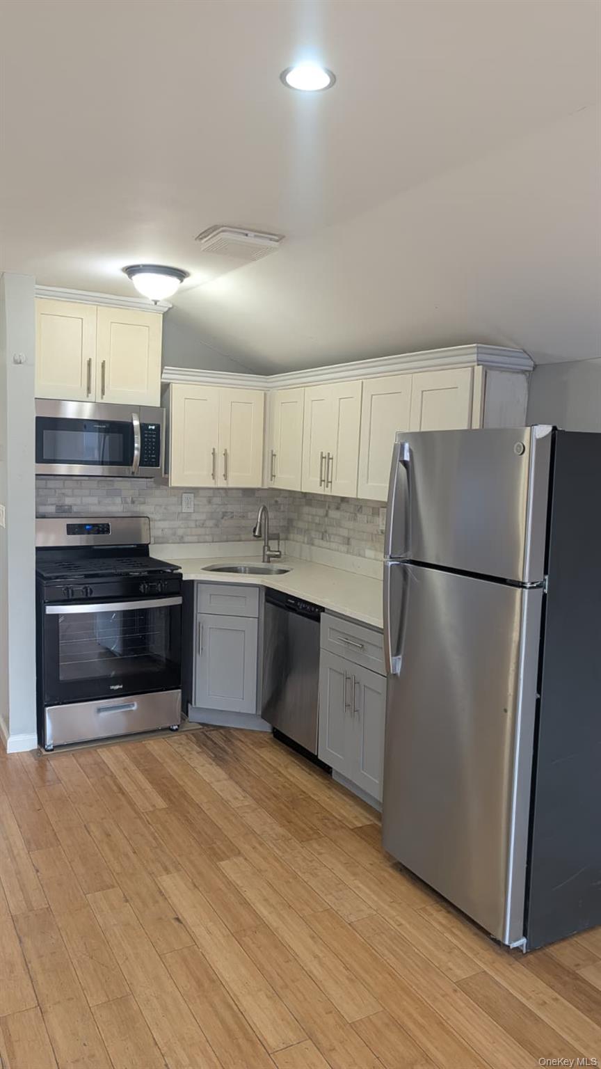 Kitchen featuring appliances with stainless steel finishes, white cabinets, vaulted ceiling, gray cabinetry, and backsplash