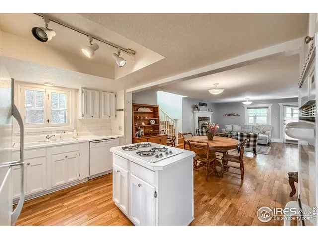 a open kitchen with stainless steel appliances granite countertop a stove top oven a sink a dining table and chairs with wooden floor