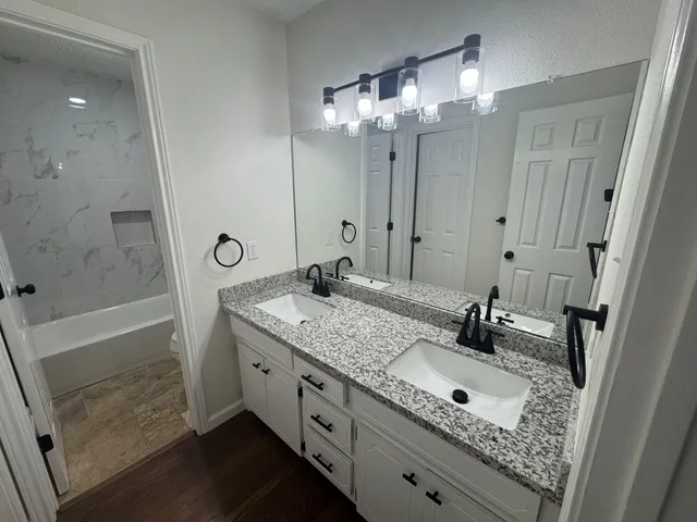 a bathroom with a sink double vanity granite tub shower and mirror
