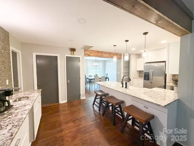 a dining hall with stainless steel appliances kitchen island granite countertop a table chairs sink and cabinets