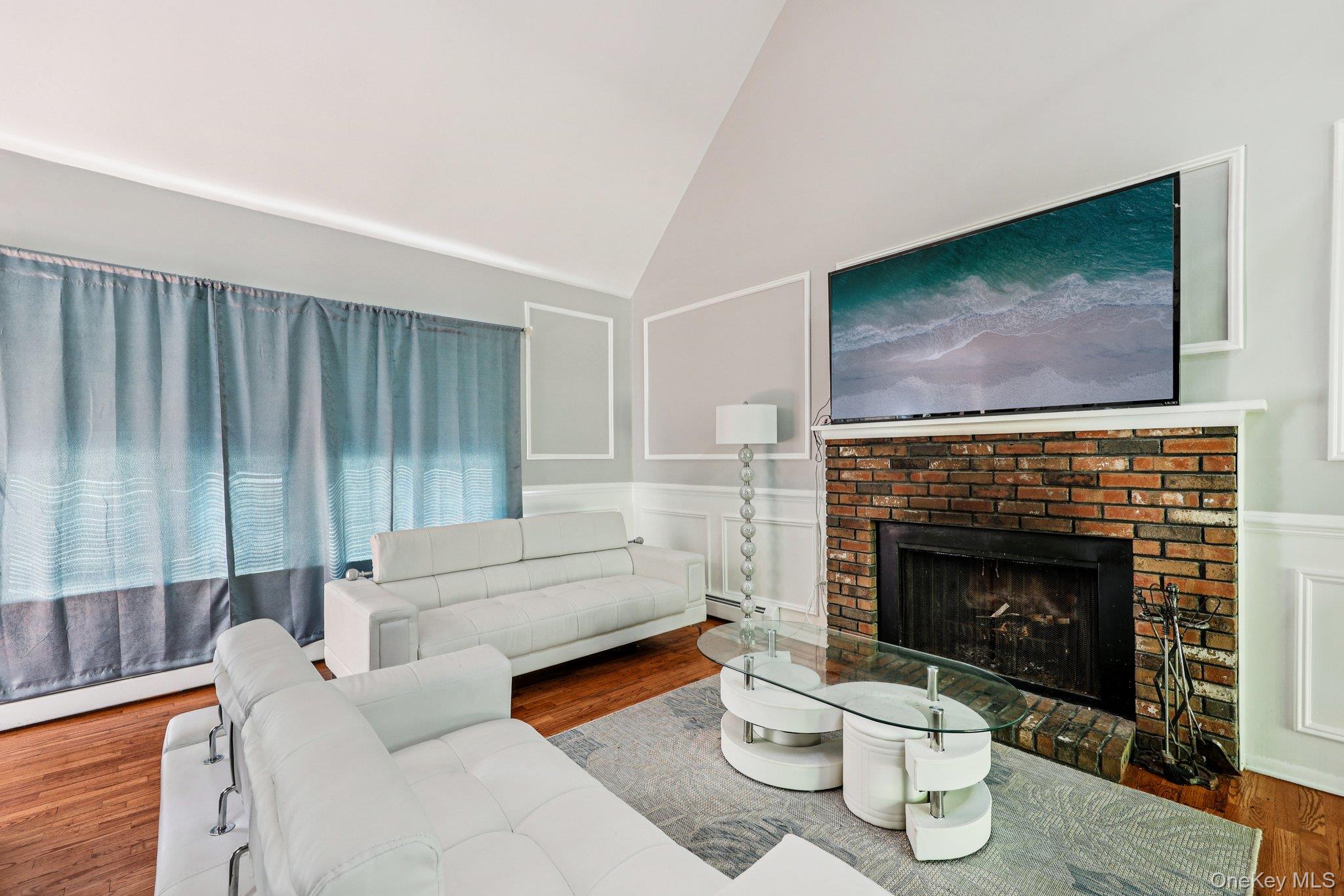 9 Crane Road Middletown, NY 10941 - Photo 3 of 31 Living room with a brick fireplace, wood finished floors, high vaulted ceiling, and wainscot walls