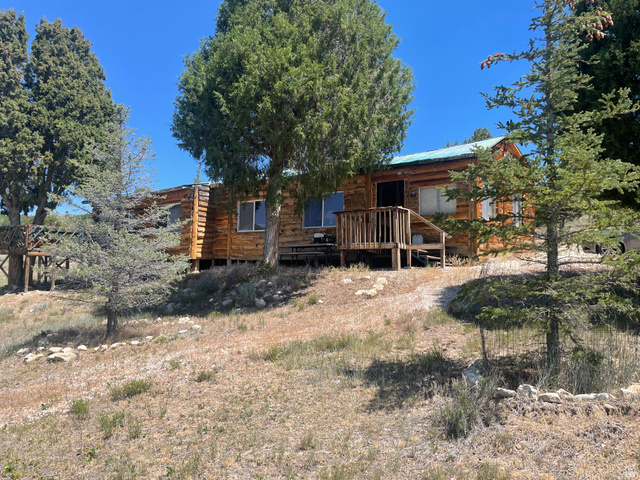 4648 West Taylor Flt Road Salina, UT 84654 - Photo 1 of 20 Rustic log cabin exterior featuring a covered porch with wooden railings, multiple windows, a metal roof, and surrounding mature trees
