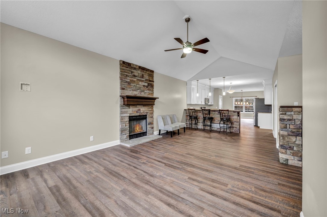 Living area featuring a stone fireplace, a chandelier, a ceiling fan, dark wood-style flooring, and vaulted ceiling