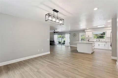 a view of an empty room and kitchen with wooden floor