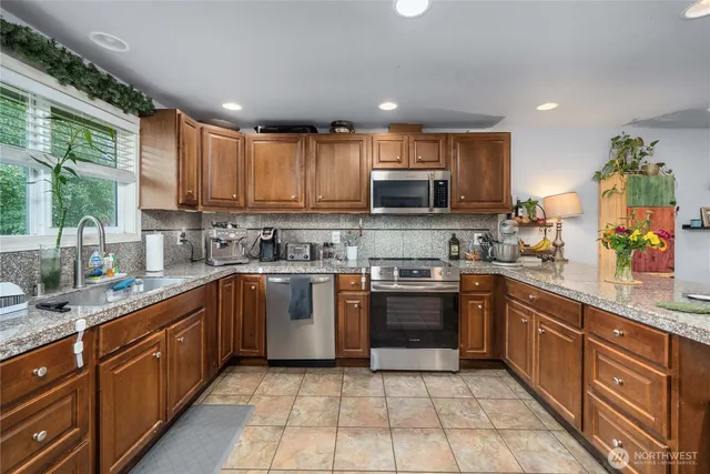 a large kitchen with stainless steel appliances granite countertop a stove top oven a sink dishwasher a dining table and chairs with wooden floor