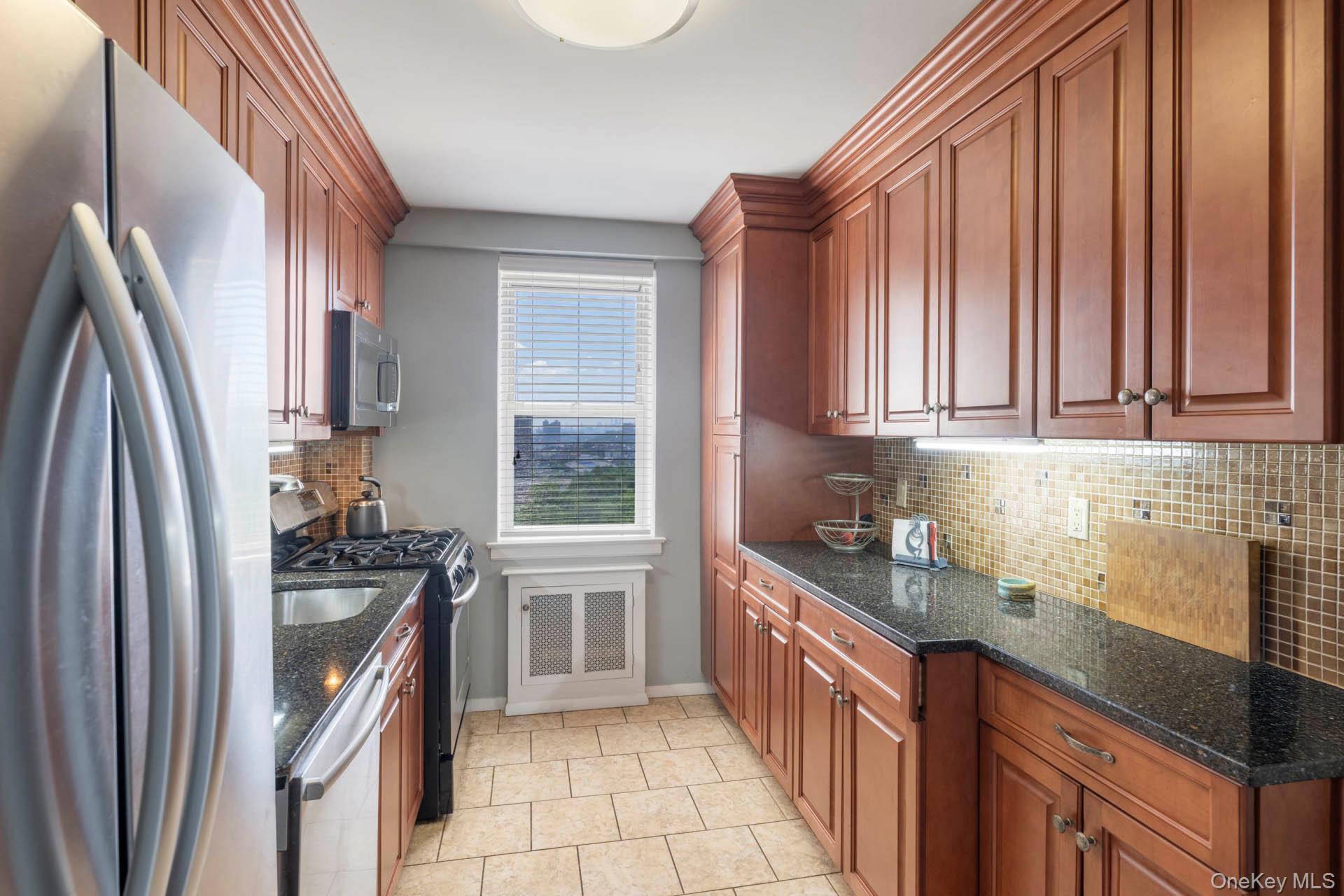 3135 Johnson Avenue, Unit 16C Bronx, NY 10463 - Photo 3 of 13 Kitchen featuring appliances with stainless steel finishes, tasteful backsplash, dark stone countertops, and brown cabinets