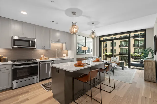 a kitchen with stainless steel appliances granite countertop a stove a refrigerator a sink a dining table and chairs with wooden floor