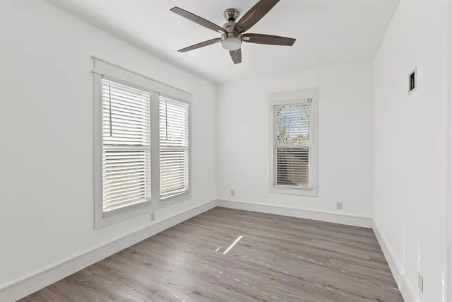 an empty room with wooden floor ceiling fan and windows