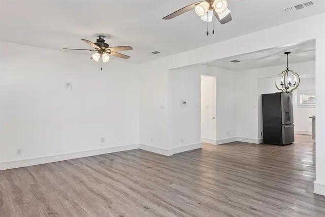a view of an empty room with wooden floor and a ceiling fan
