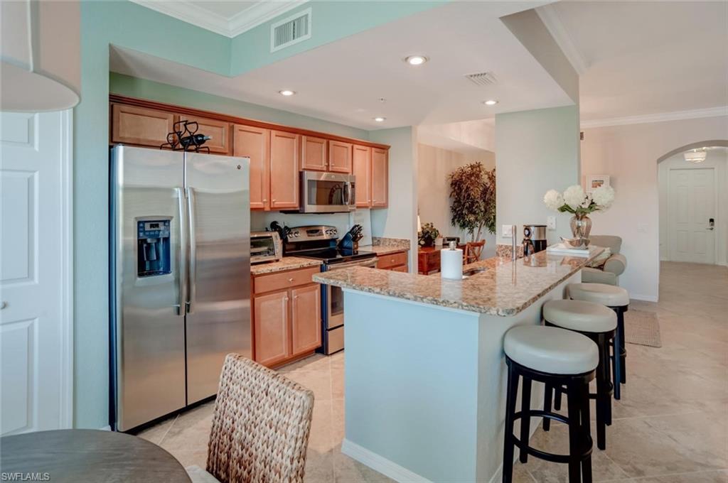 9731 Acqua Court, Unit 523 Naples, FL 34113 - Photo 7 of 27 a kitchen with stainless steel appliances granite countertop a refrigerator a stove a sink a dining table and chairs with wooden floor