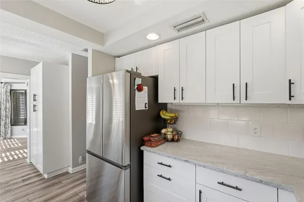 a kitchen with stainless steel appliances granite countertop a refrigerator a sink and white cabinets with wooden floor