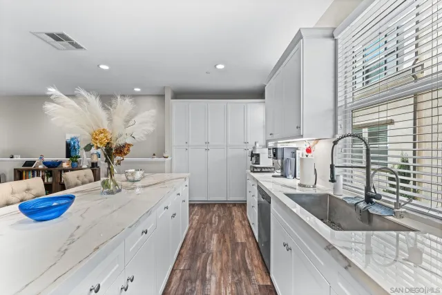 a kitchen with stainless steel appliances kitchen island granite countertop a sink dishwasher and white cabinets with wooden floor