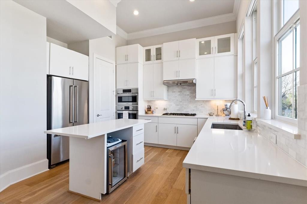 4129 Runyon Road Addison, TX 75001 - Photo 12 of 38 Kitchen featuring stainless steel appliances, white cabinetry, glass fronted cabinets, a center island, and tasteful backsplash