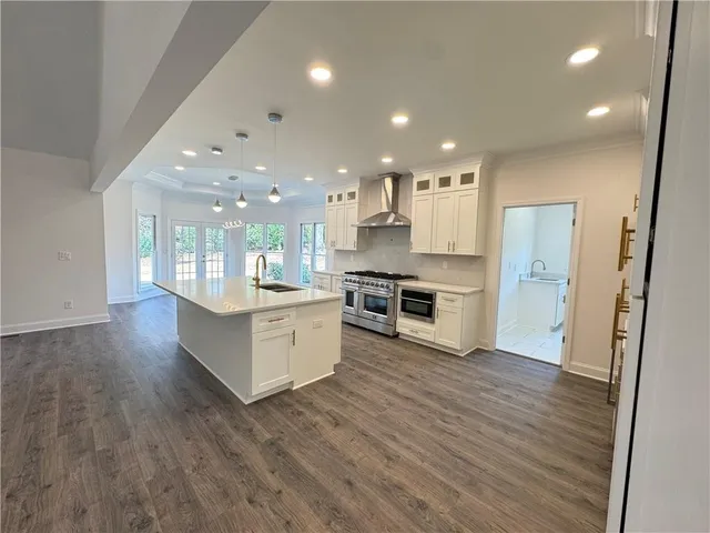 a large kitchen with kitchen island a stove a sink dishwasher a refrigerator and white cabinets with wooden floor