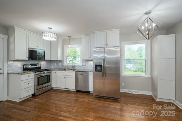 a kitchen with stainless steel appliances granite countertop a refrigerator a stove a sink and a white cabinets