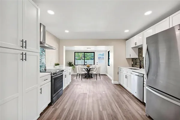 a kitchen with granite countertop stainless steel appliances a stove refrigerator a sink dishwasher a dining table and chairs with wooden floor