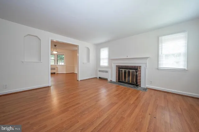 an empty room with wooden floor fireplace and windows