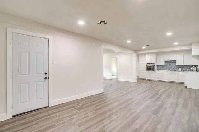 a view of an empty room and kitchen with wooden floor