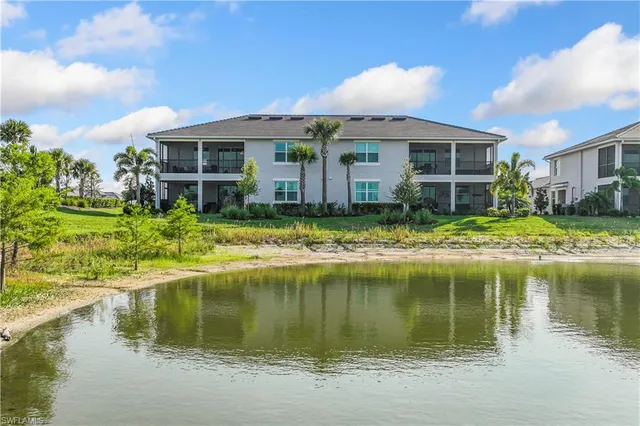 a view of a lake with a house and a yard with potted plants and large trees