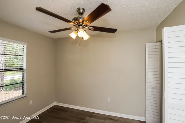 an empty room with wooden floor fan and windows