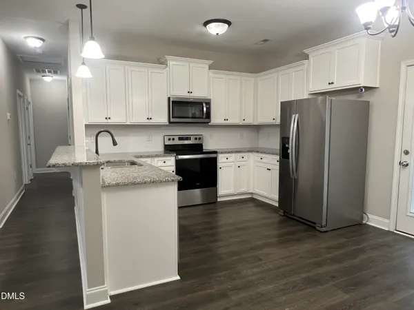 a kitchen with stainless steel appliances granite countertop a refrigerator a stove a sink and white cabinets with wooden floor