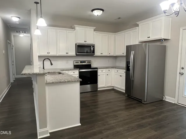 a kitchen with stainless steel appliances granite countertop a refrigerator a stove a sink and white cabinets with wooden floor